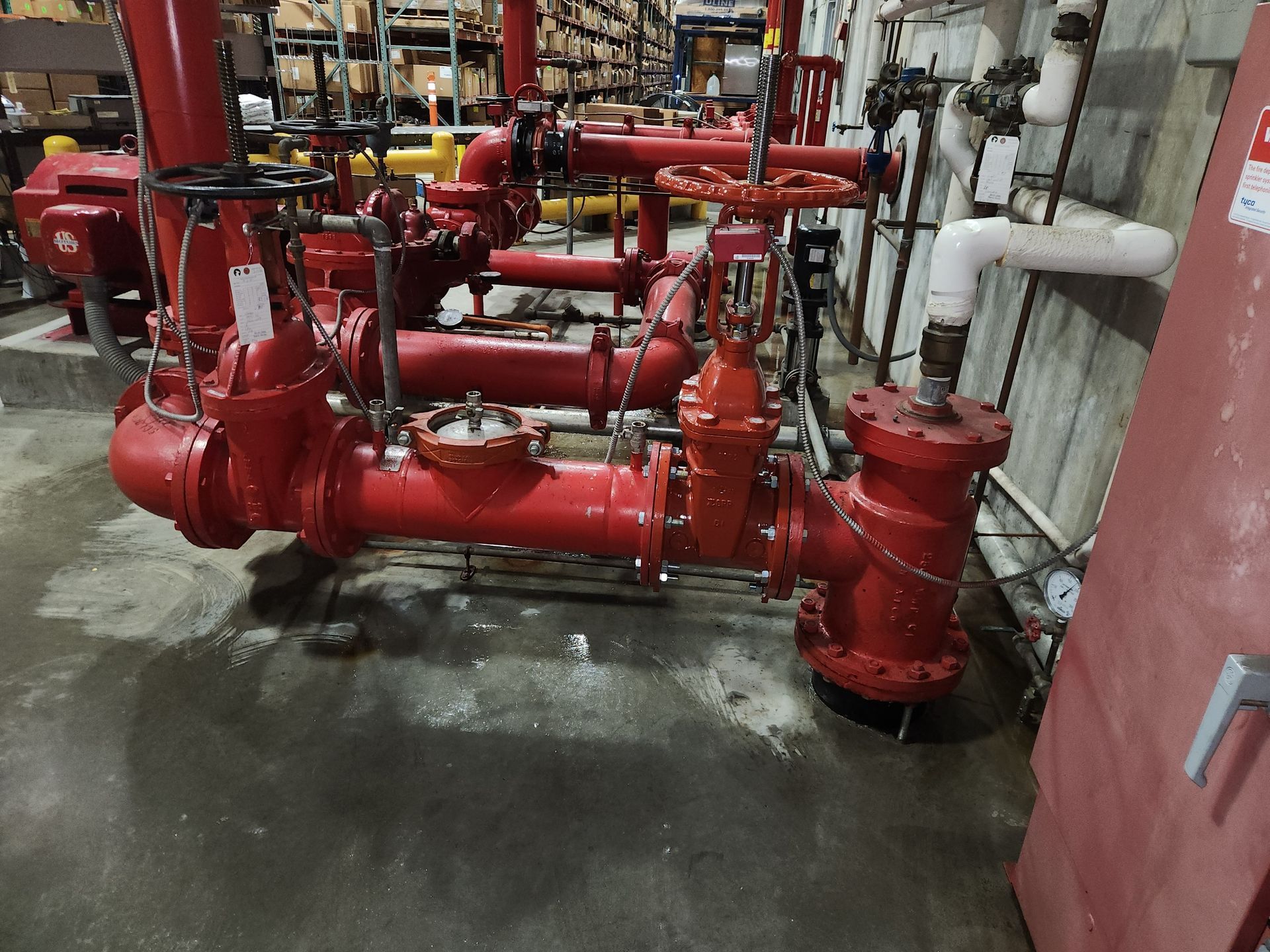 Red commercial fire-sprinkler riser with OS&Y valves, gauges, and flanged piping in a warehouse mechanical room